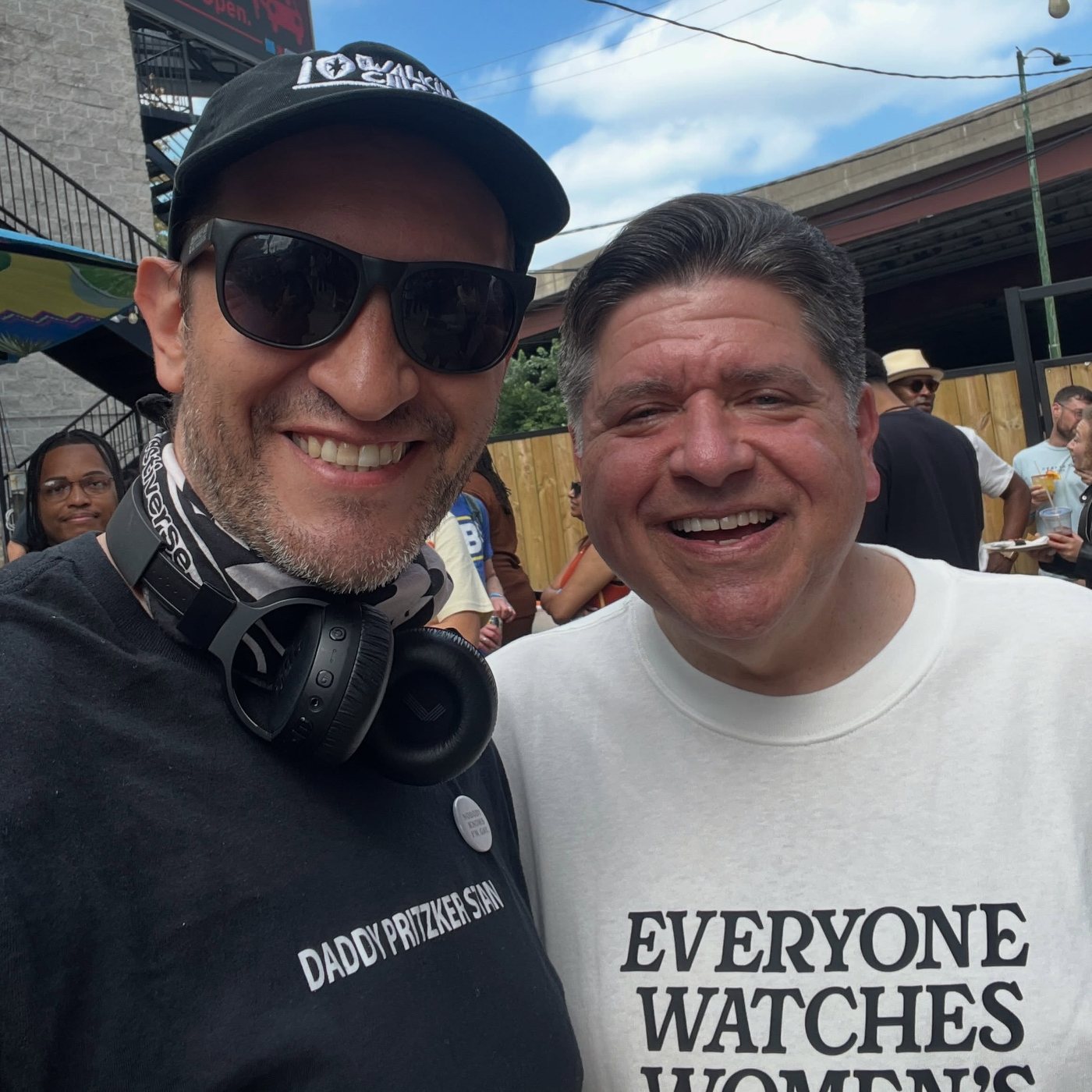Vitaliy Vladimirov in sunglasses and a Walking Chicago cap, smiling alongside Illinois Governor JB Pritzker at an outdoor event